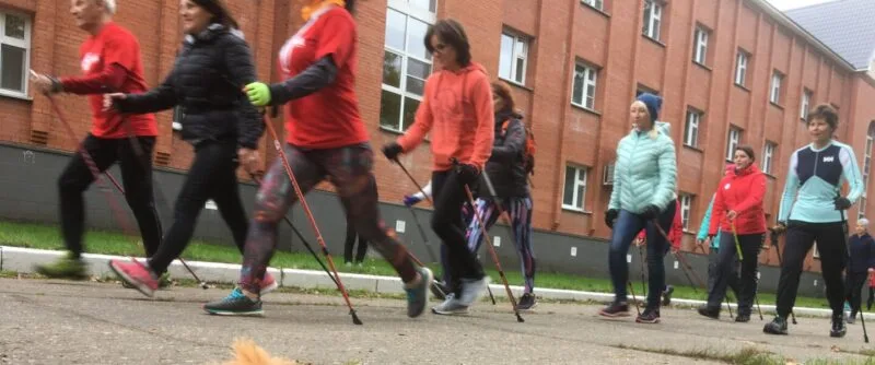Grup de adulți care merg alert pe o alee, cu bețe de nordic walking