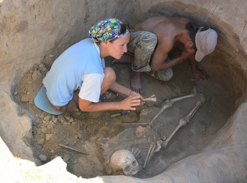 Arheologi lucrând cu un schelet într-un mormânt, în timpul unor săpături
