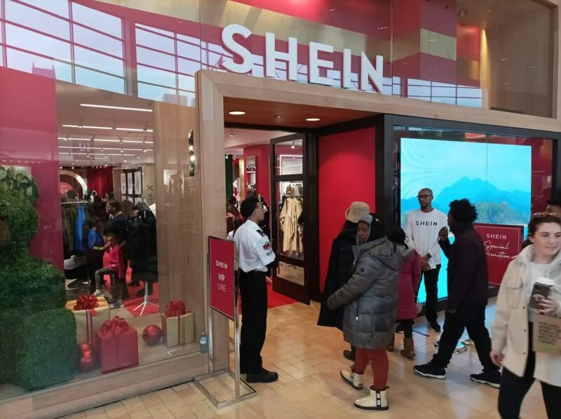 Interiorul unui magazin pop-up Shein, cu rafturi de haine și logo-ul brandului
