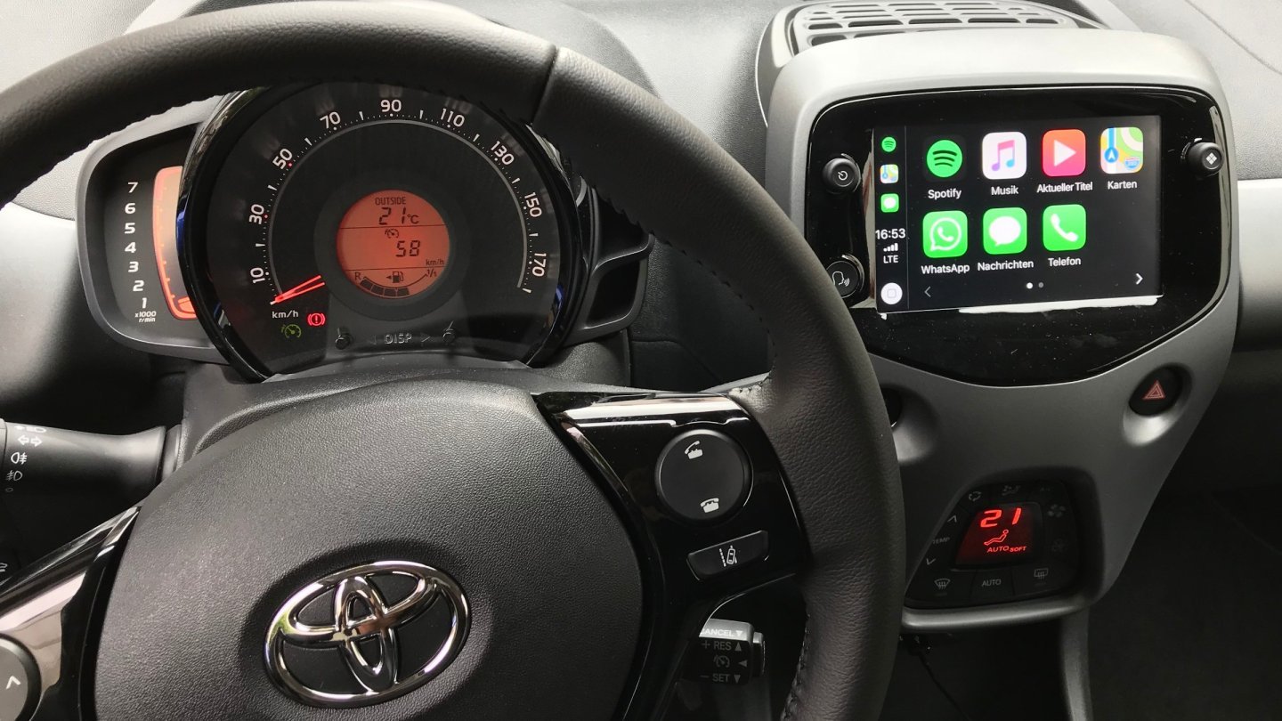 Bordul unei mașini de oraș, cu volanul în prim-plan și ecranul central care afișează interfața Apple CarPlay
