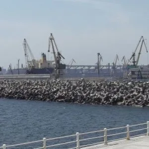 stabilopodul românesc Dig din port acoperit cu blocuri de beton, cu macarale portuare în fundal