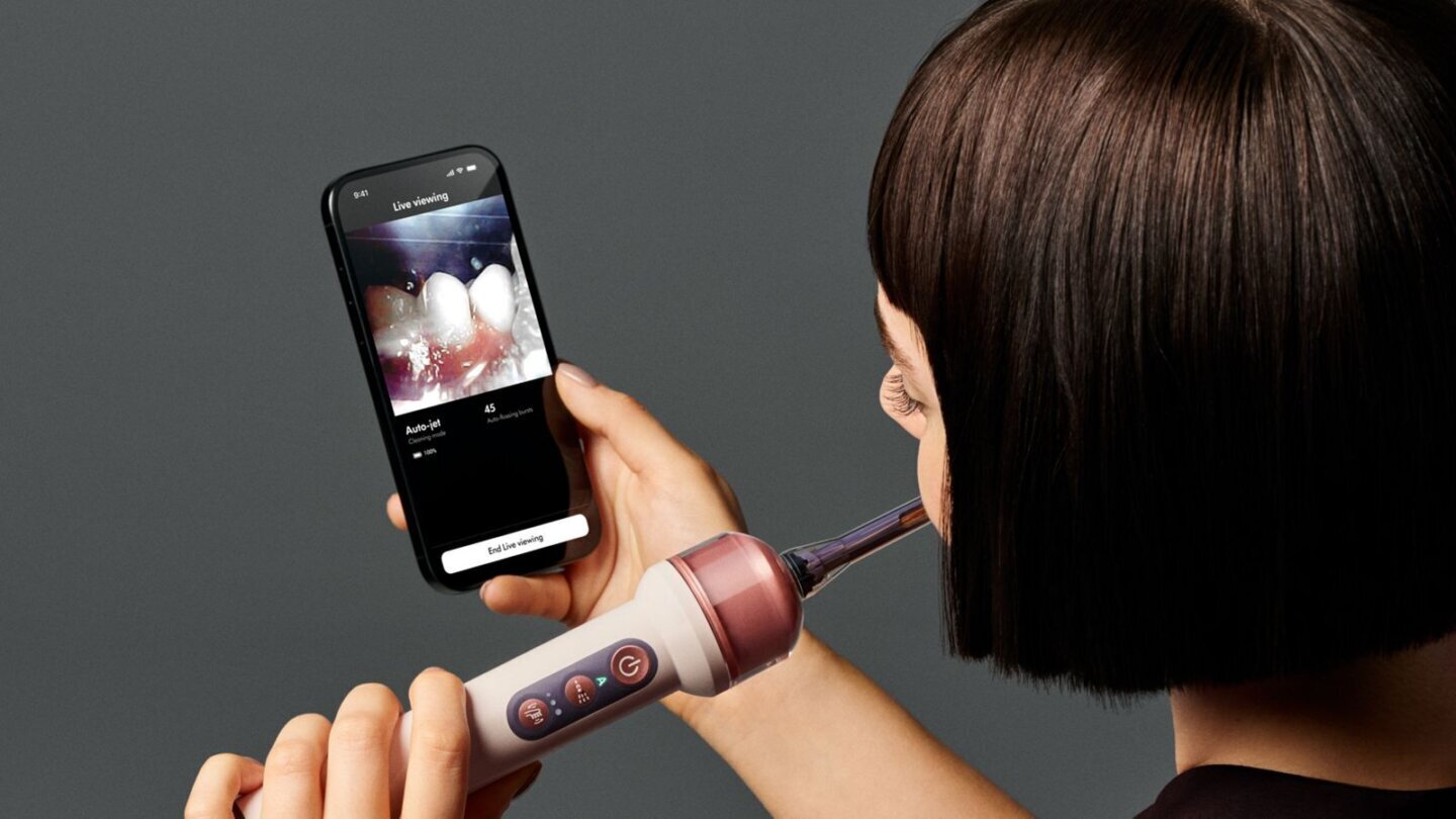 Utilizatoare care se spală pe dinți cu Dyson CameraJet în timp ce pe telefon se vede transmisia live din interiorul gurii în aplicația MyDyson