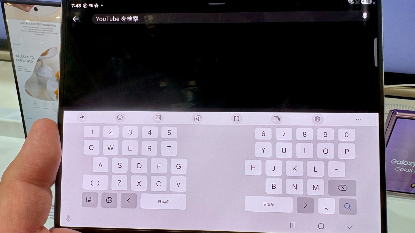 Mână care ține un Galaxy Z Fold8 deschis în mod peisaj, cu tastatura virtuală împărțită în două pe ecranul interior lat