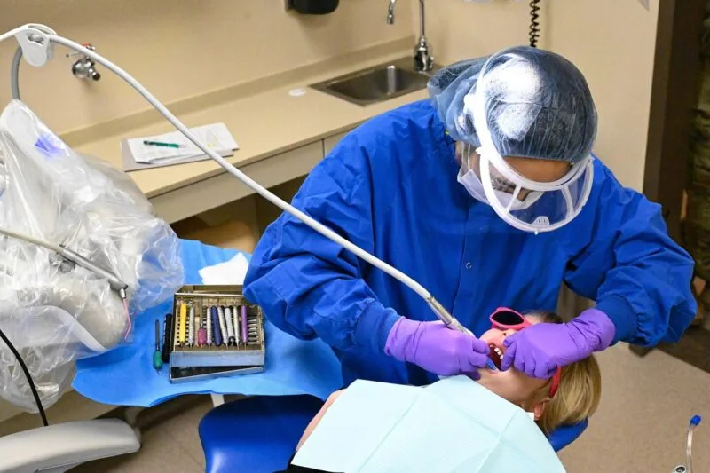 Igienist dentar curăță dinții unui pacient întins pe scaunul stomatologic