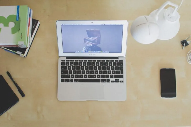 Laptop deschis pe un birou de lemn, lângă un caiet
