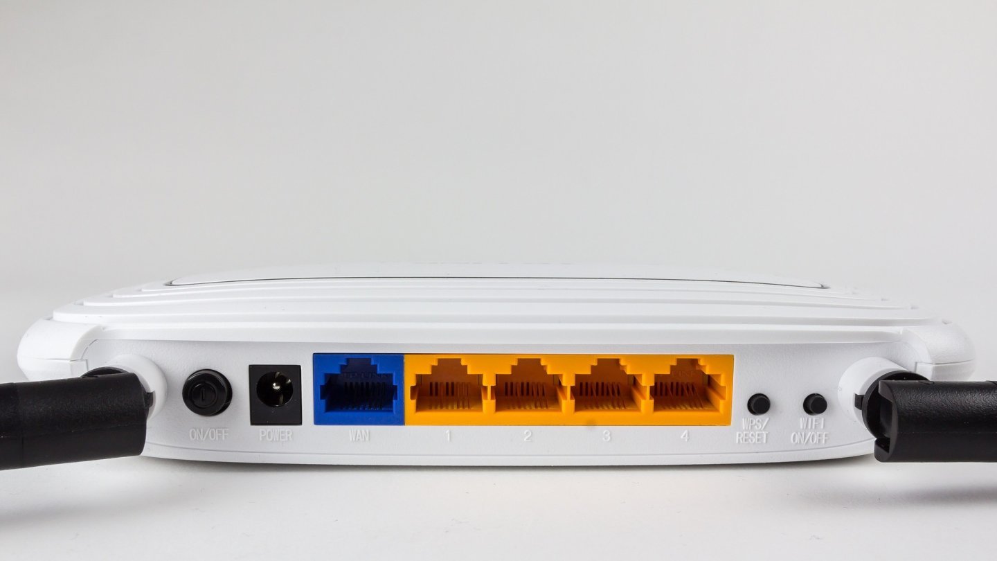 Spatele unui router wireless alb cu port WAN albastru, patru porturi LAN galbene, buton de resetare și mufa de alimentare