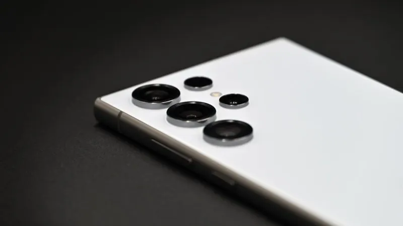 Spatele alb al unui Samsung Galaxy S24 Ultra, cu cele patru camere și blițul, pe fundal închis