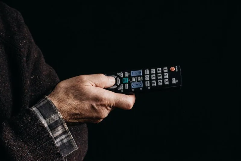 Persoană care ține o telecomandă într-o cameră slab luminată, pregătindu-se să pornească un serial