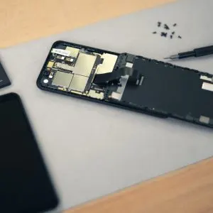 Smartphone demontat pe o masă: ecranul, bateria scoasă, placa de bază și o șurubelniță cu șuruburi mici alături