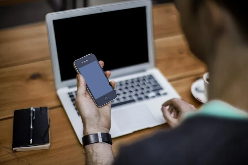 Persoană care folosește un laptop și un telefon, într-un spațiu de lucru