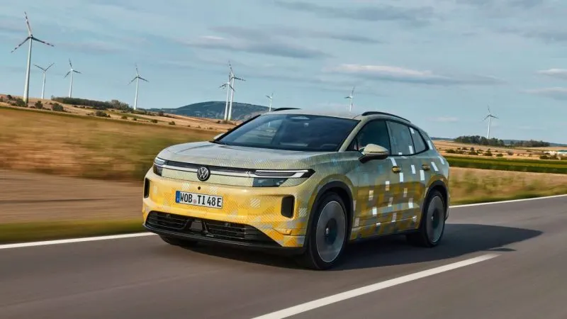 Prototipul Volkswagen ID. Tiguan cu folie de camuflaj galbenă, rulând pe un drum de țară, cu turbine eoliene în fundal