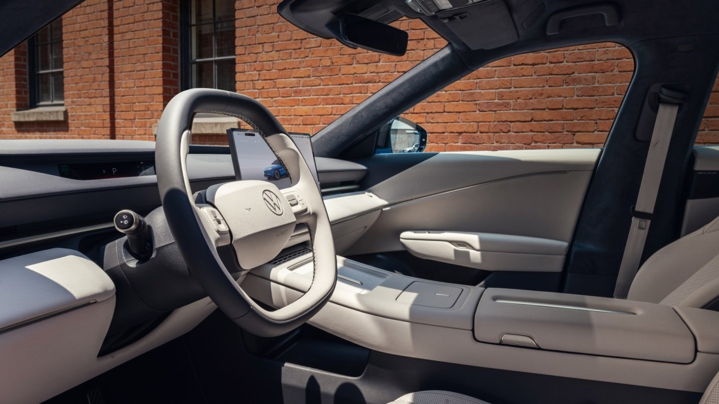 Habitaclul Volkswagen ID. UNYX 09 văzut prin portiera șoferului: volan cu două spițe, bord deschis la culoare și ecran central flotant