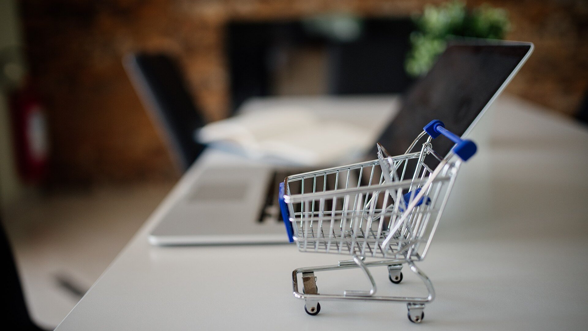 Coș de cumpărături în miniatură lângă un laptop, pentru cumpărăturile online de Black Friday