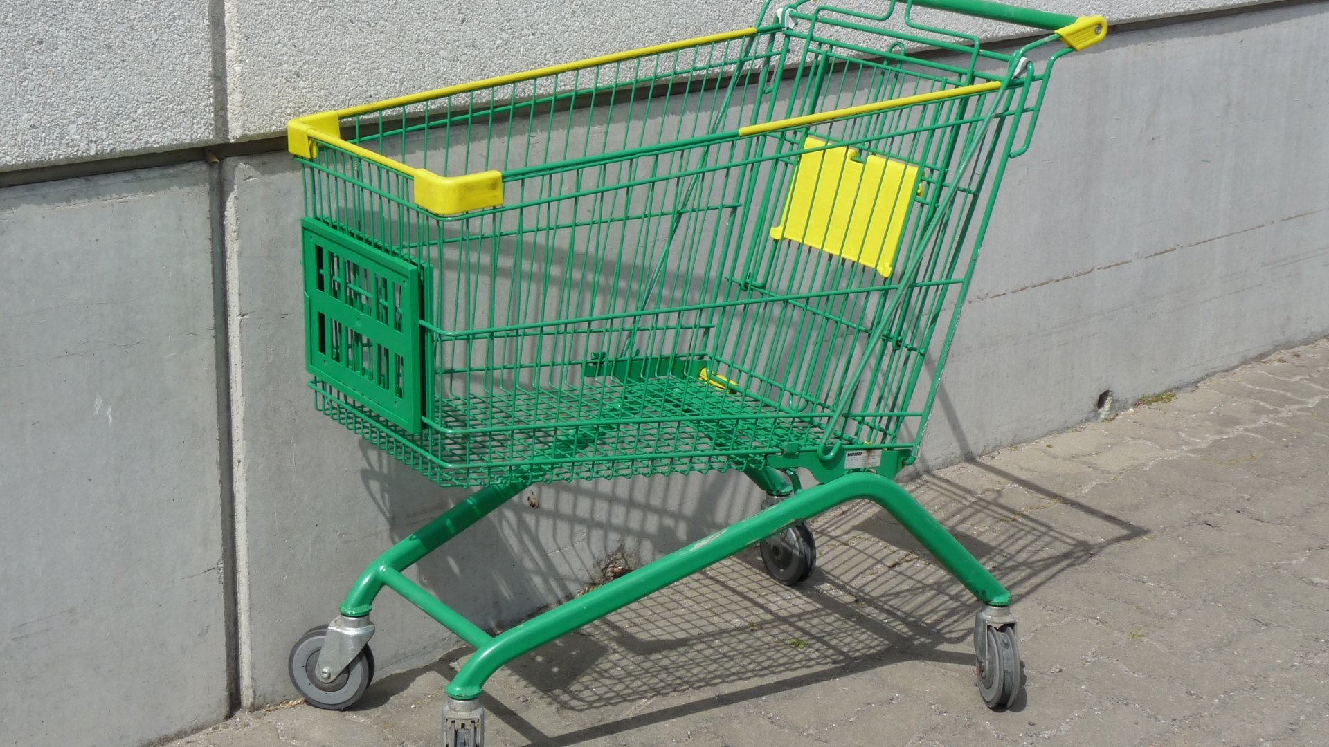 Cărucior de cumpărături verde sprijinit de peretele unui supermarket