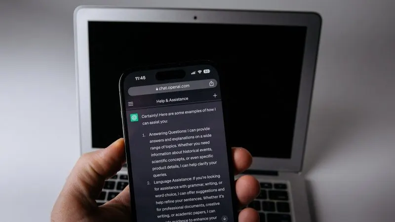 ChatGPT Slides Telefon cu aplicația ChatGPT deschisă, ținut în mână în fața unui laptop