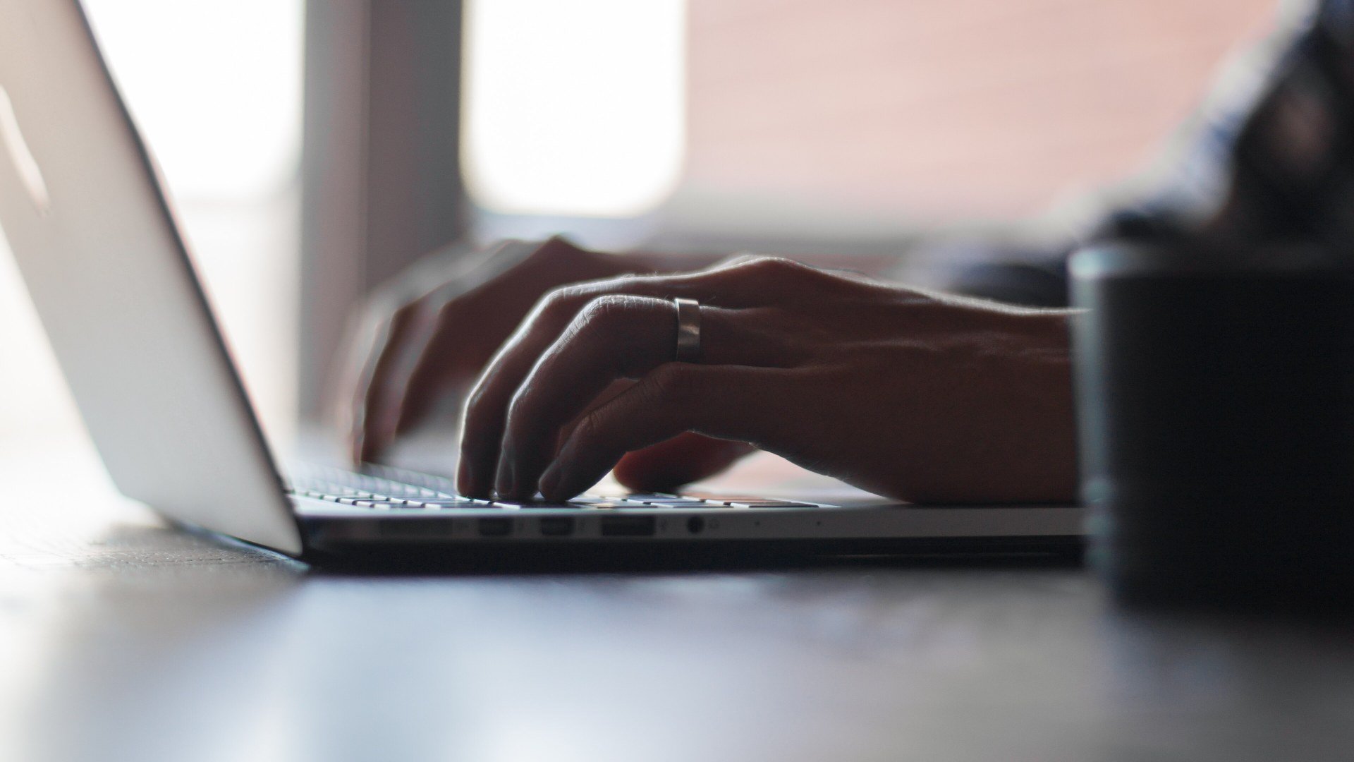 Escrocherii ClickFix: mâinile unei persoane care tastează la un laptop, pe un birou, într-o încăpere luminoasă