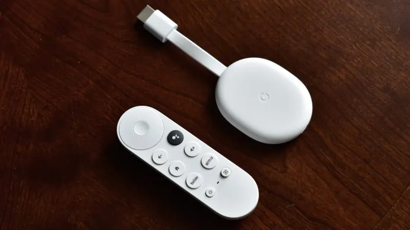 Dispozitiv de streaming Chromecast with Google TV alb, cu telecomanda Bluetooth, pe o masă din lemn