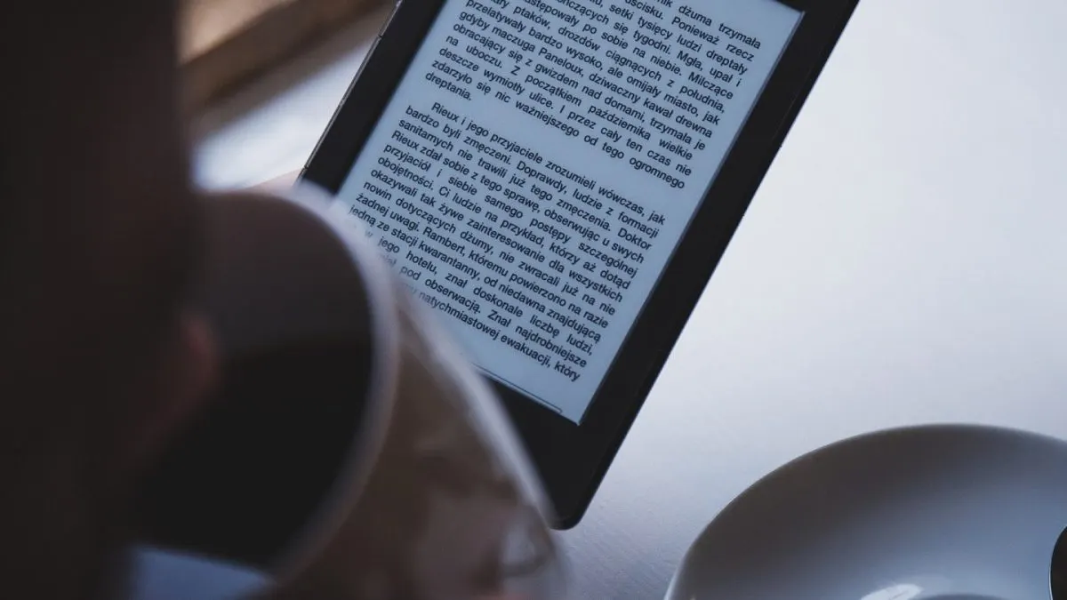 Kindle 2026 Persoană care citește pe un e-reader cu ecran e-ink, ținut în mână deasupra unei mese