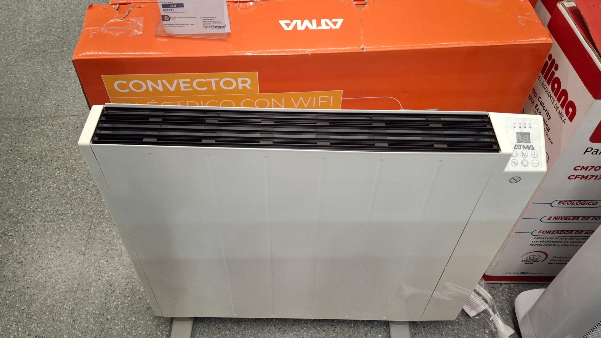 Convector electric alb de podea, expus pe raft într-un magazin, lângă cutii