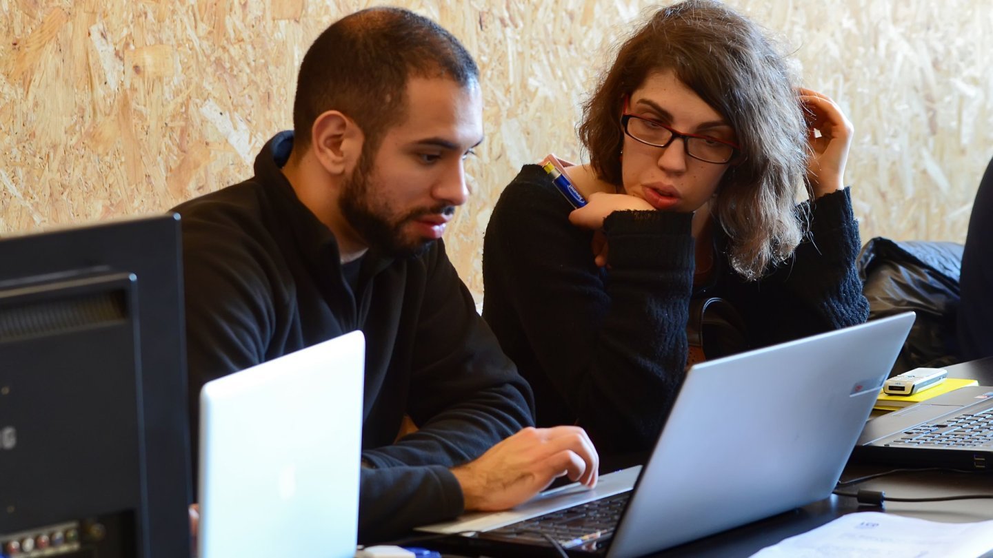 Un bărbat și o femeie privesc împreună ecranul unui laptop în timpul unui maraton de creare a jocurilor