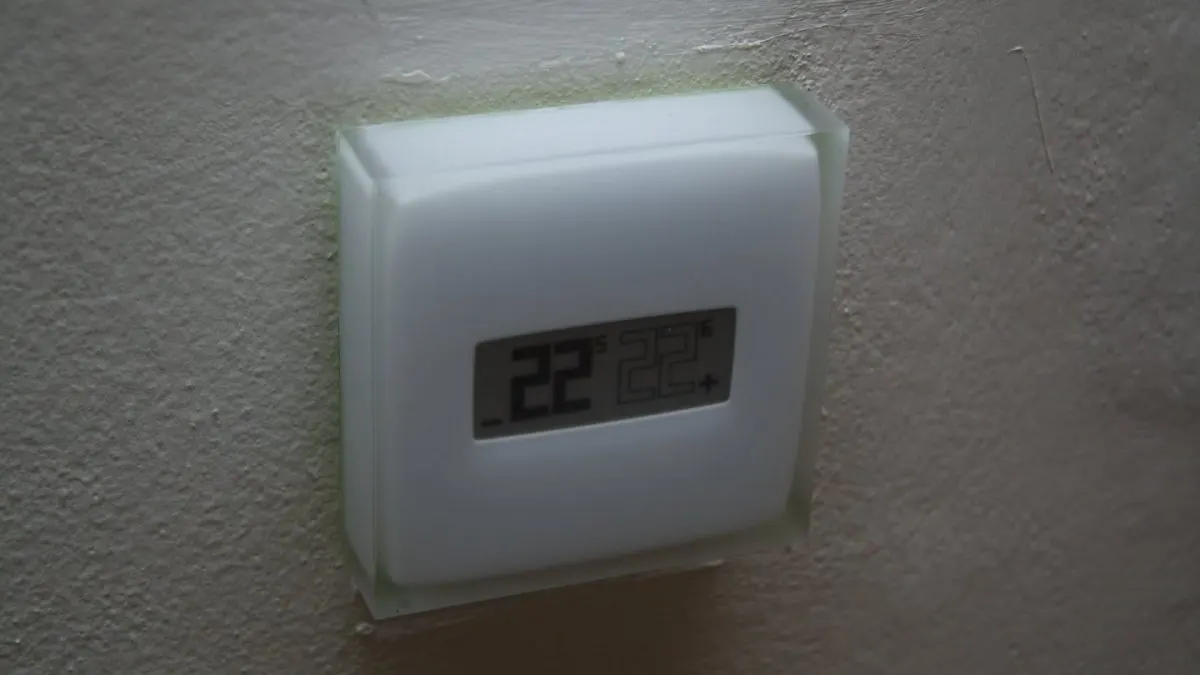 dispozitive smart home Termostat inteligent alb, cu ecran care afișează temperatura, montat pe un perete deschis la culoare
