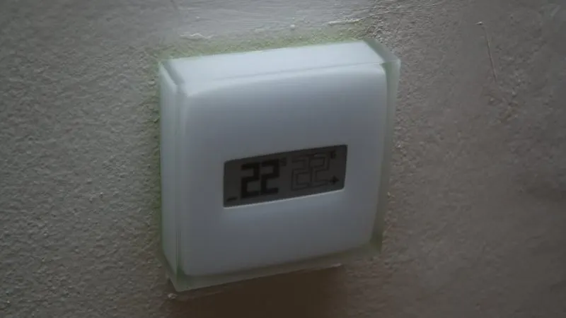 Termostat inteligent alb, cu ecran care afișează temperatura, montat pe un perete deschis la culoare