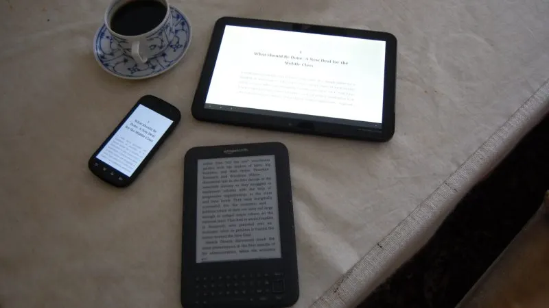 Cititor de cărți electronice cu ecran E Ink așezat lângă o tabletă, un telefon și o ceașcă de cafea