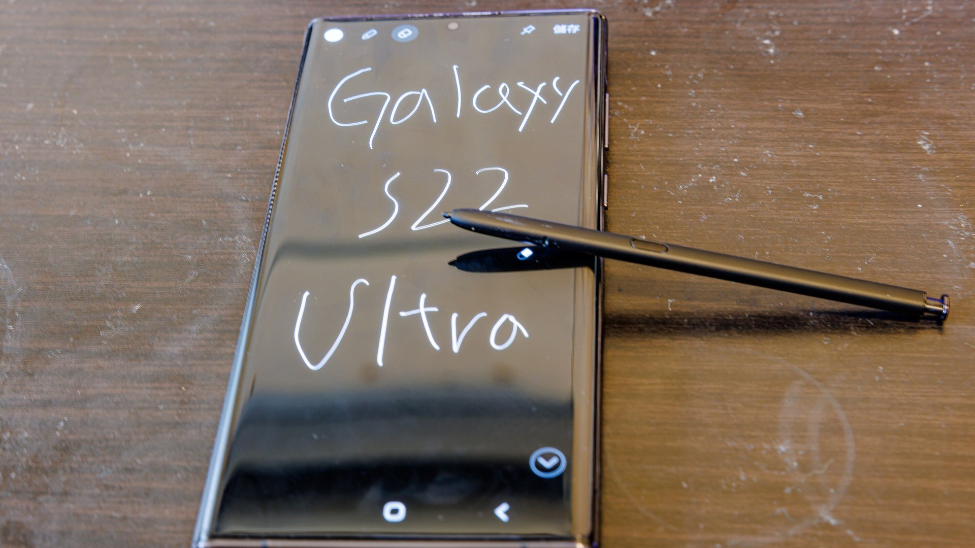 Galaxy S22 Ultra negru cu S Pen pe o masă de lemn, telefon afectat de limitarea GOS în jocuri