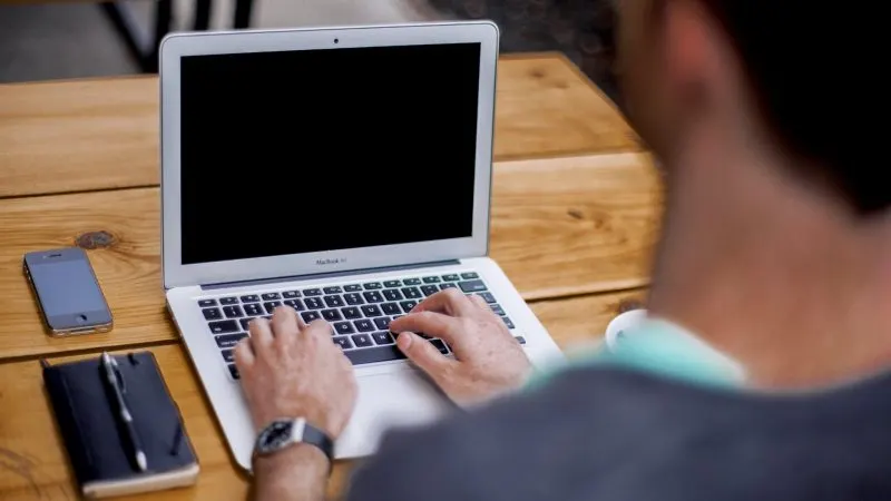 Bărbat care scrie la un laptop pe o masă de lemn