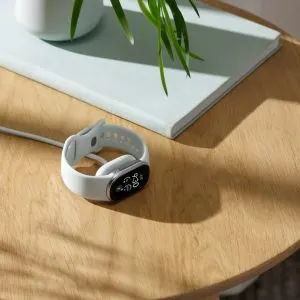 Brățara Google Fitbit Edge argintie, așezată pe o masă de lemn lângă încărcătorul magnetic