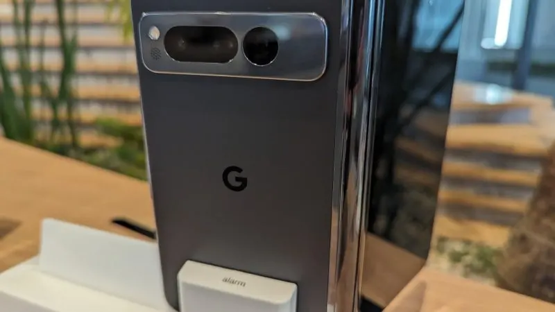 Telefonul pliabil Google Pixel Fold gri, văzut din spate cu modulul de camere, pe un stand de prezentare