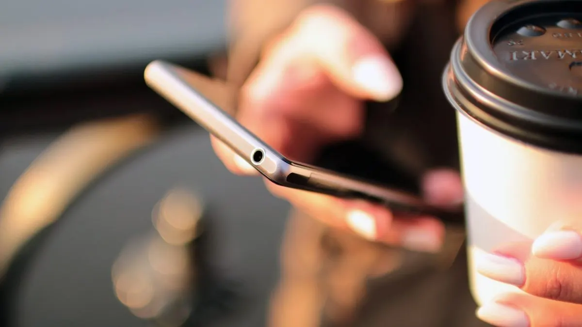 Google Play Persoană care folosește un telefon Android, ținând o cafea în cealaltă mână