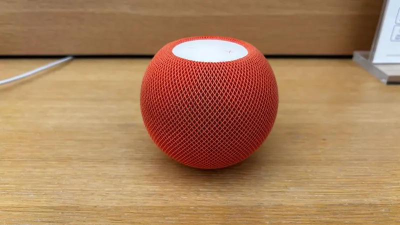 Boxă inteligentă Apple HomePod mini în culoarea portocaliu, pe o suprafață din lemn