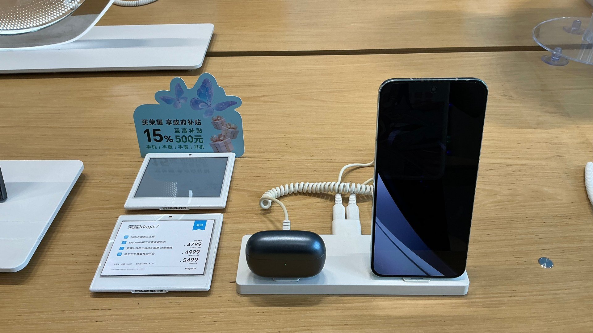 Telefonul HONOR Magic7 pe un suport de prezentare, lângă o pereche de căști wireless