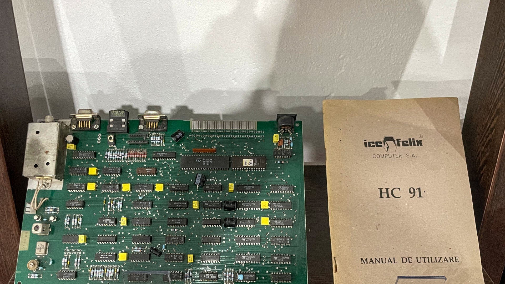 Placa de bază verde a unui calculator românesc ICE Felix HC 91, alături de manualul de utilizare original