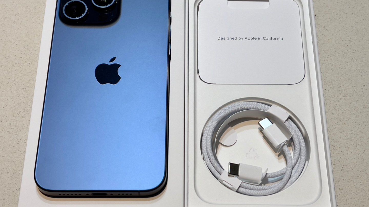 calitatea apelurilor pe iPhone Un iPhone 15 Pro Max albastru, așezat lângă cutia originală și cablul USB-C