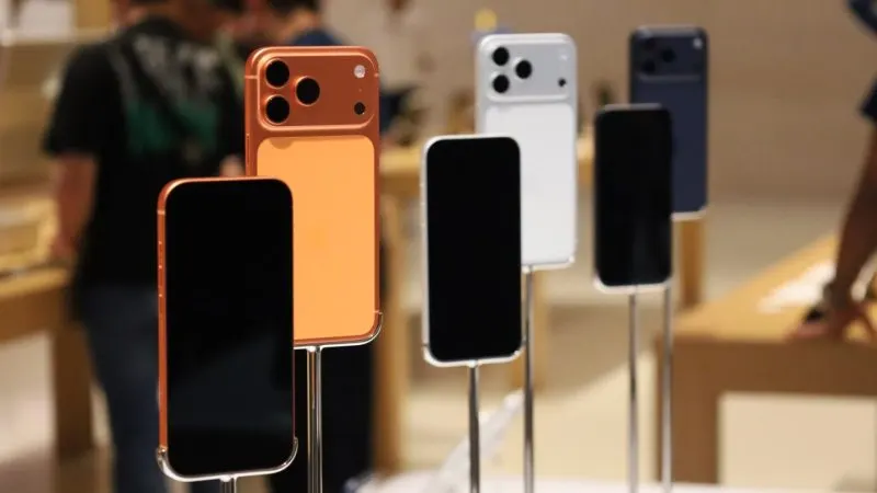 Mai multe telefoane iPhone 17 în culori diferite, prinse pe suporturi metalice de prezentare într-un magazin Apple