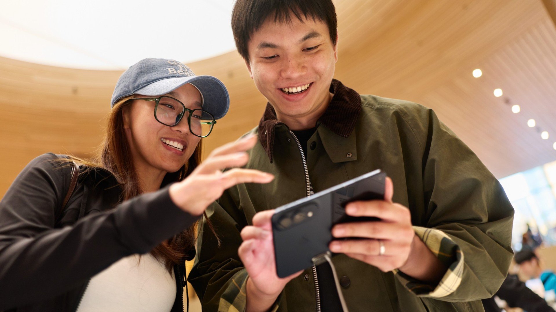 Doi clienți care testează un iPhone Duo negru, deschis, într-un magazin Apple