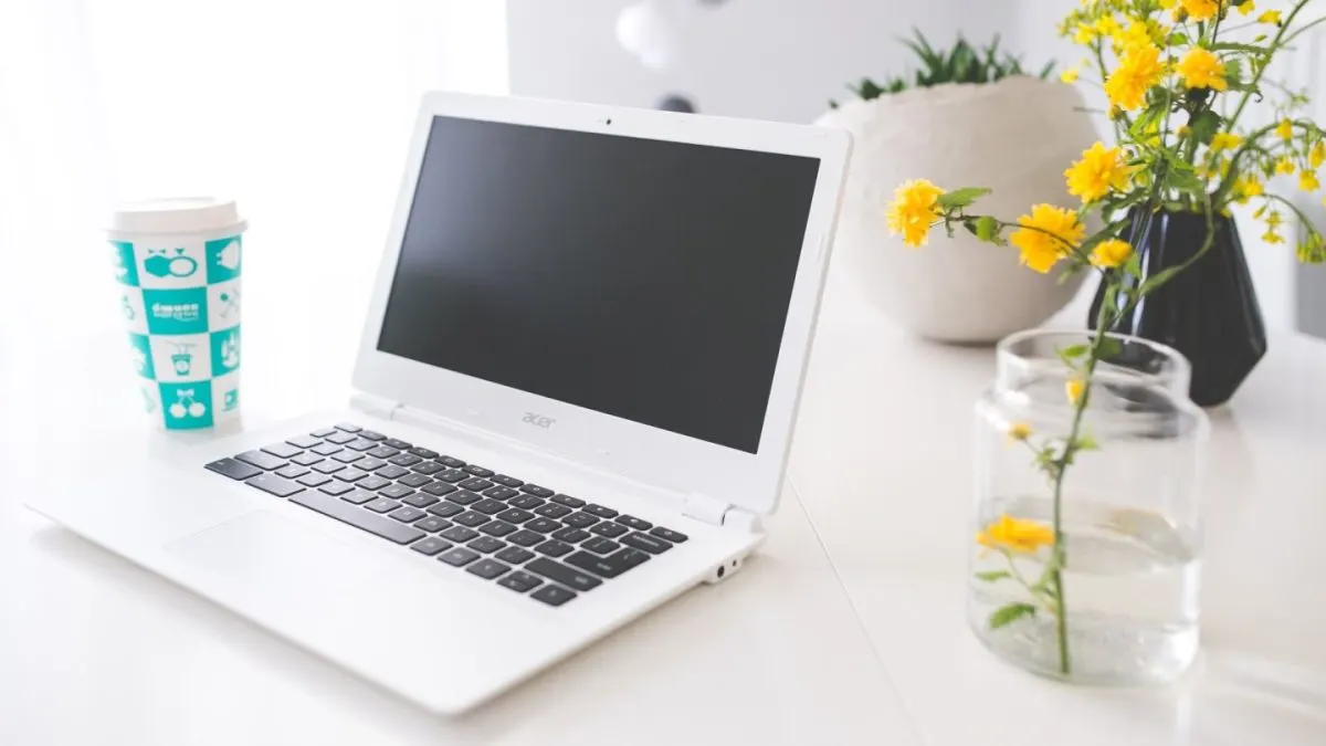 consum baterie laptop Un laptop alb deschis pe un birou, lângă o vază cu flori galbene și o cană