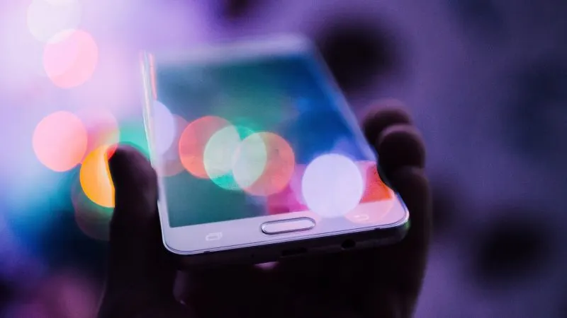 Smartphone ținut în mână pe un fundal cu lumini estompate, ilustrând scăderea livrărilor de smartphone-uri