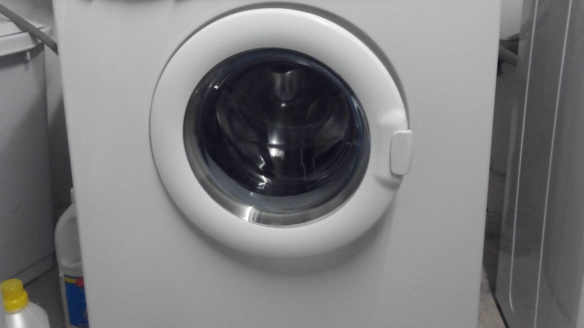 Mașină de spălat rufe albă cu încărcare frontală, instalată într-o baie