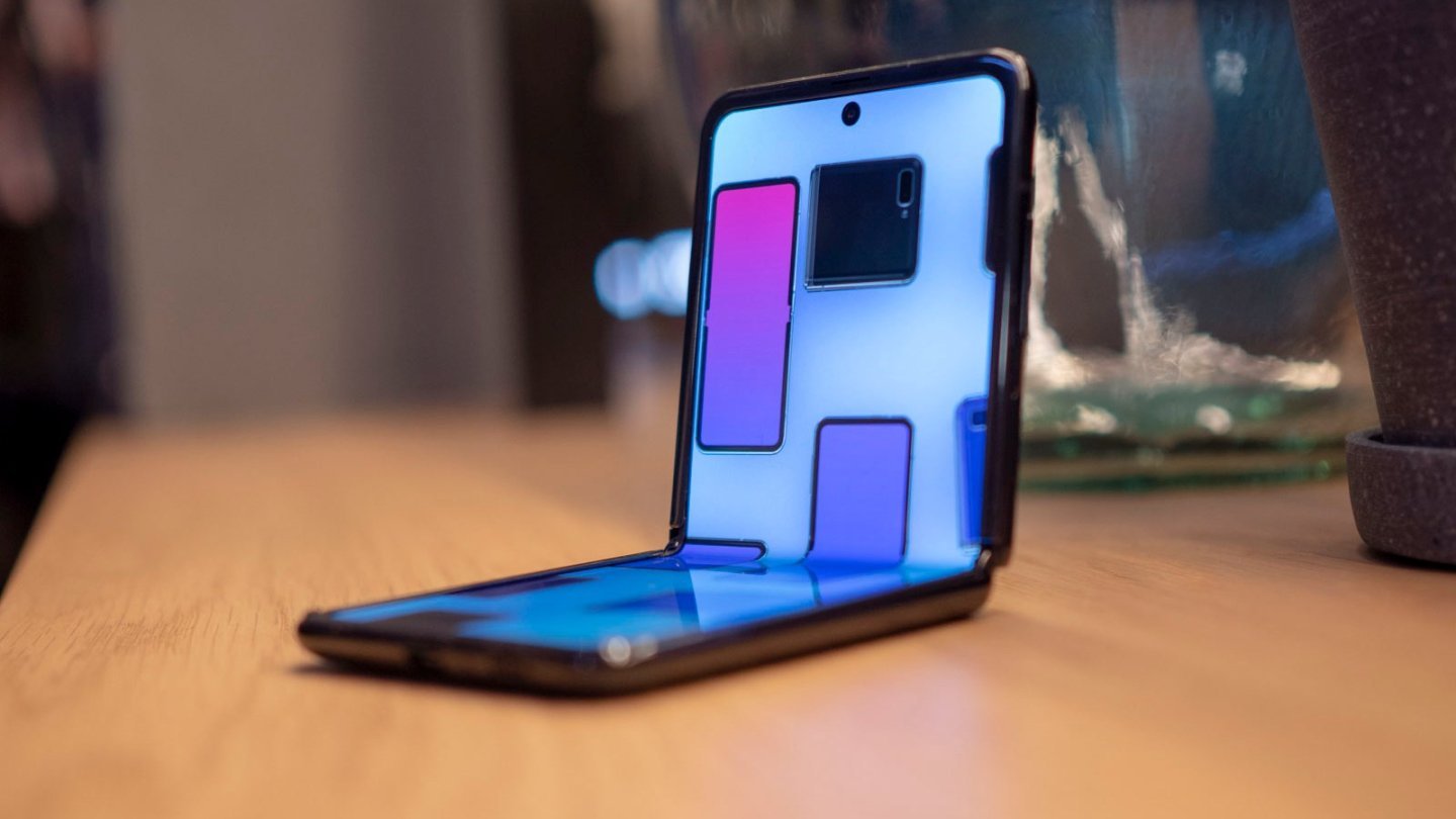 telefon pliabil Un Samsung Galaxy Z Flip mov pliat la jumătate, în modul Flex, pe o masă de lemn