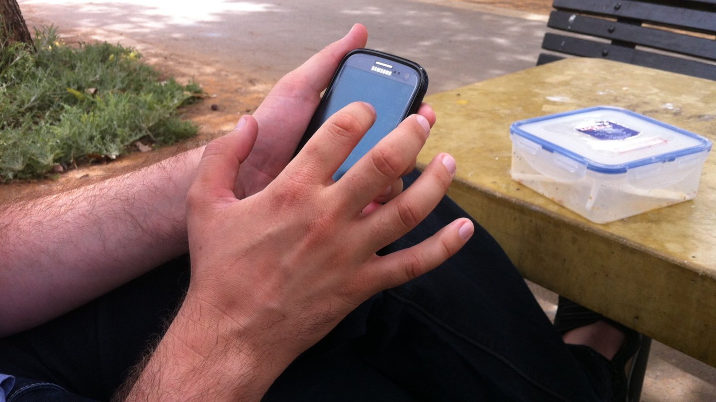 Gemini Notebook Mâinile unei persoane care folosește un smartphone la o masă în aer liber, lângă o grădină