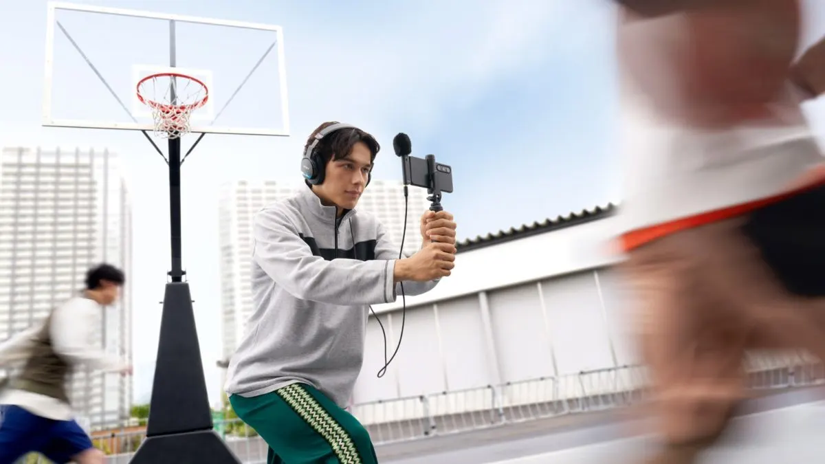 Sony ECM-AX10 Creator de conținut care filmează cu telefonul pe un gimbal, cu microfonul Sony ECM-AX10 atașat, pe un teren de baschet