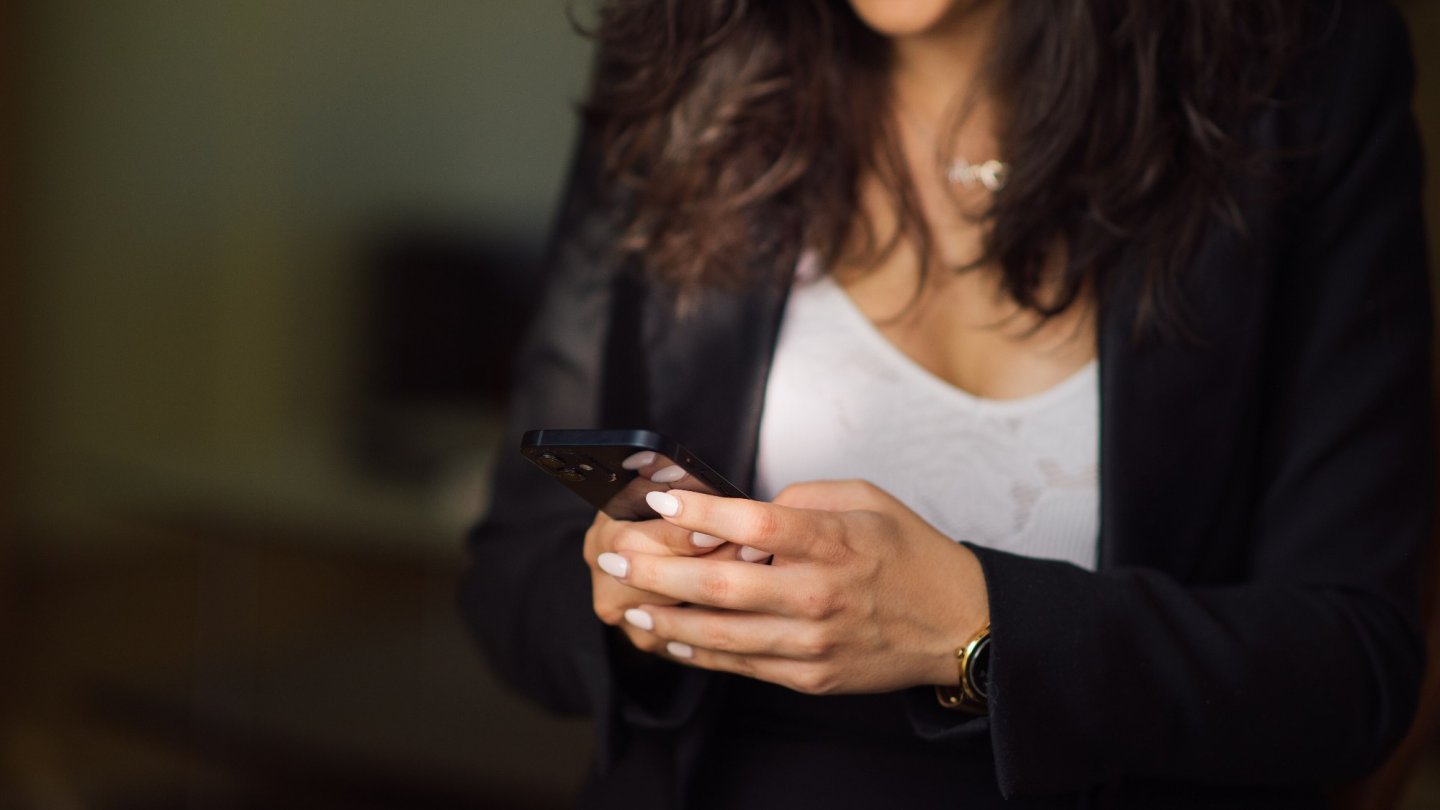 actualizarea aplicațiilor O femeie cu părul creț care ține un smartphone în ambele mâini și se uită la ecran