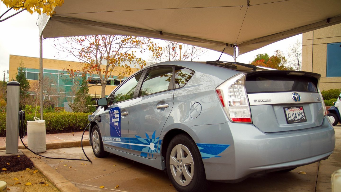 ce înseamnă PHEV O Toyota Prius Plug-in Hybrid argintie conectată la o stație de încărcare sub un cort